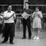 A cheerful black and white photo of three adults smiling and clapping indoors in Ciudad de México.