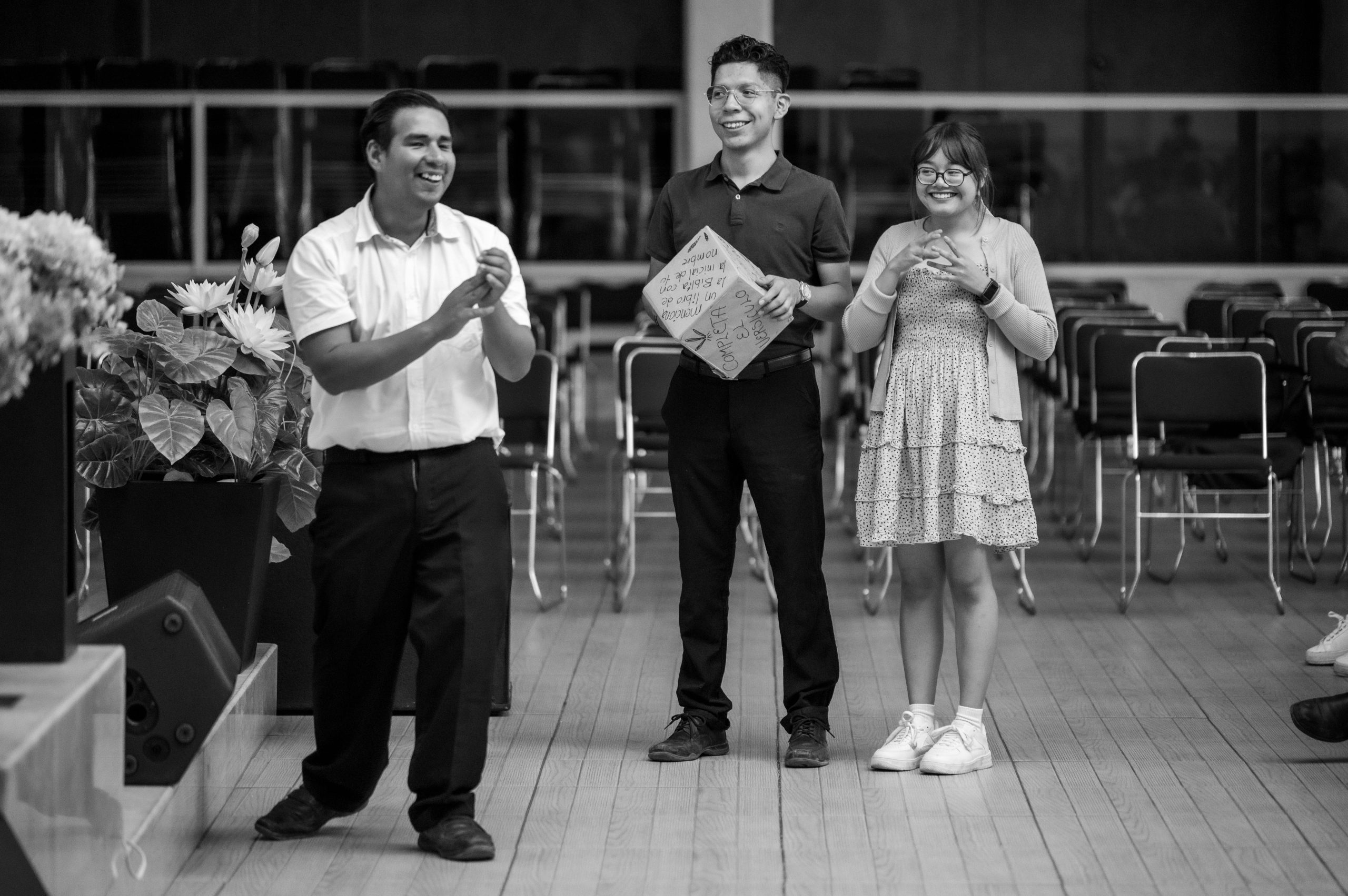 A cheerful black and white photo of three adults smiling and clapping indoors in Ciudad de México.