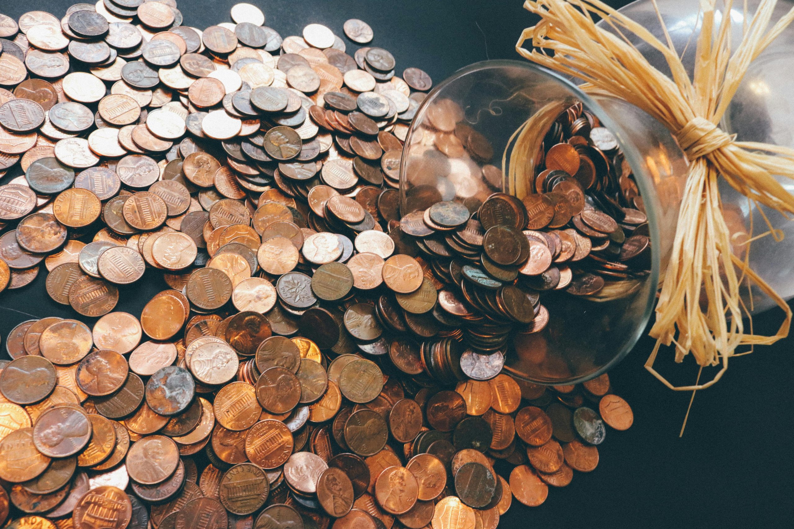 لماذا تفشل بعض العملات رغم قوة اقتصادها 2 Spilled jar of pennies creating a pattern of coins representing savings and finance.