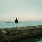 A contemplative woman stands on a pier, looking out at the tranquil sea in Chiba, Japan.