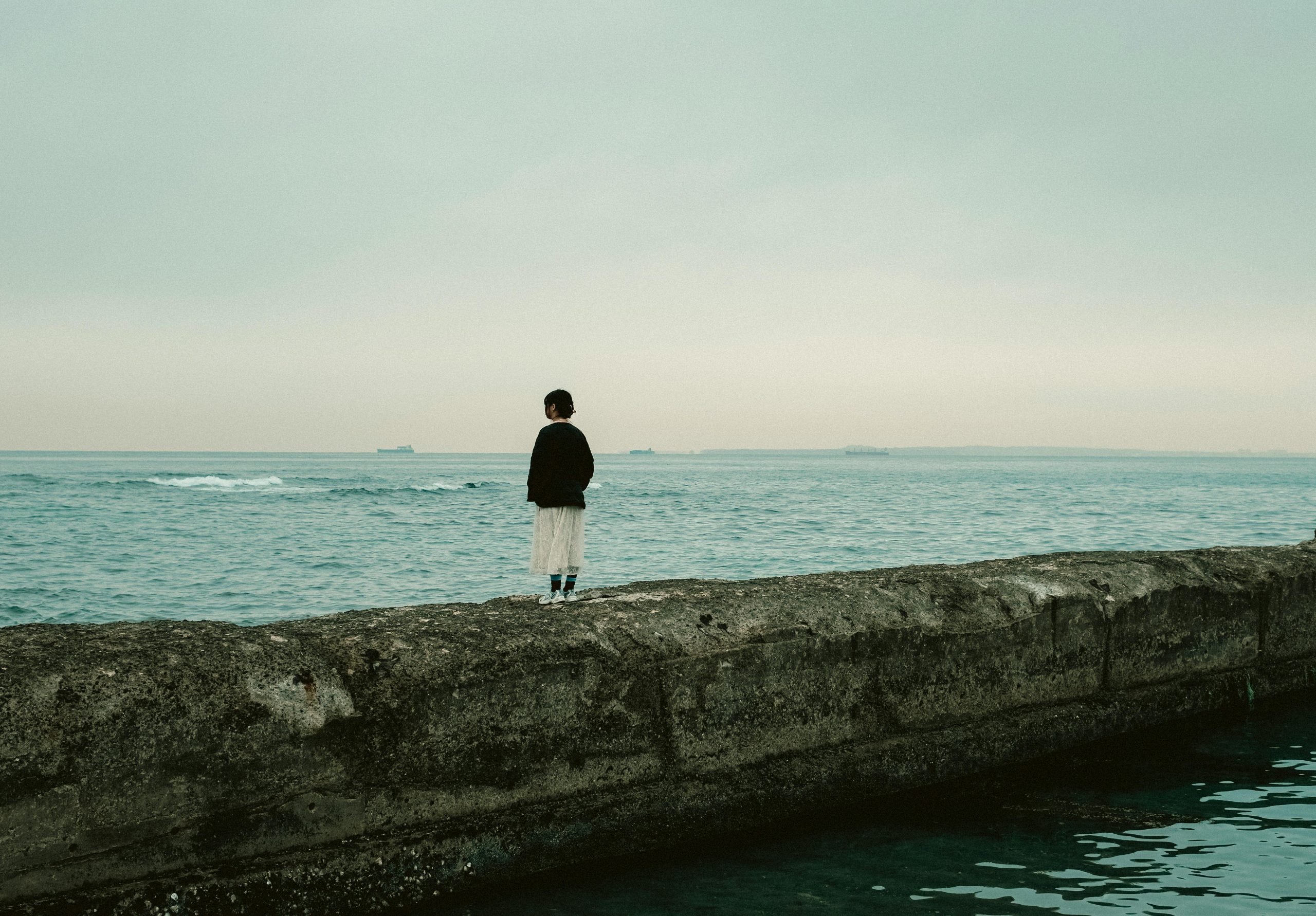 A contemplative woman stands on a pier, looking out at the tranquil sea in Chiba, Japan.