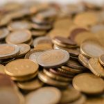 A variety of Euro coins scattered on a flat surface, showcasing different denominations in a warm light.