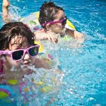 Two young girls enjoying a playful day in a bright blue swimming pool with colorful float rings.