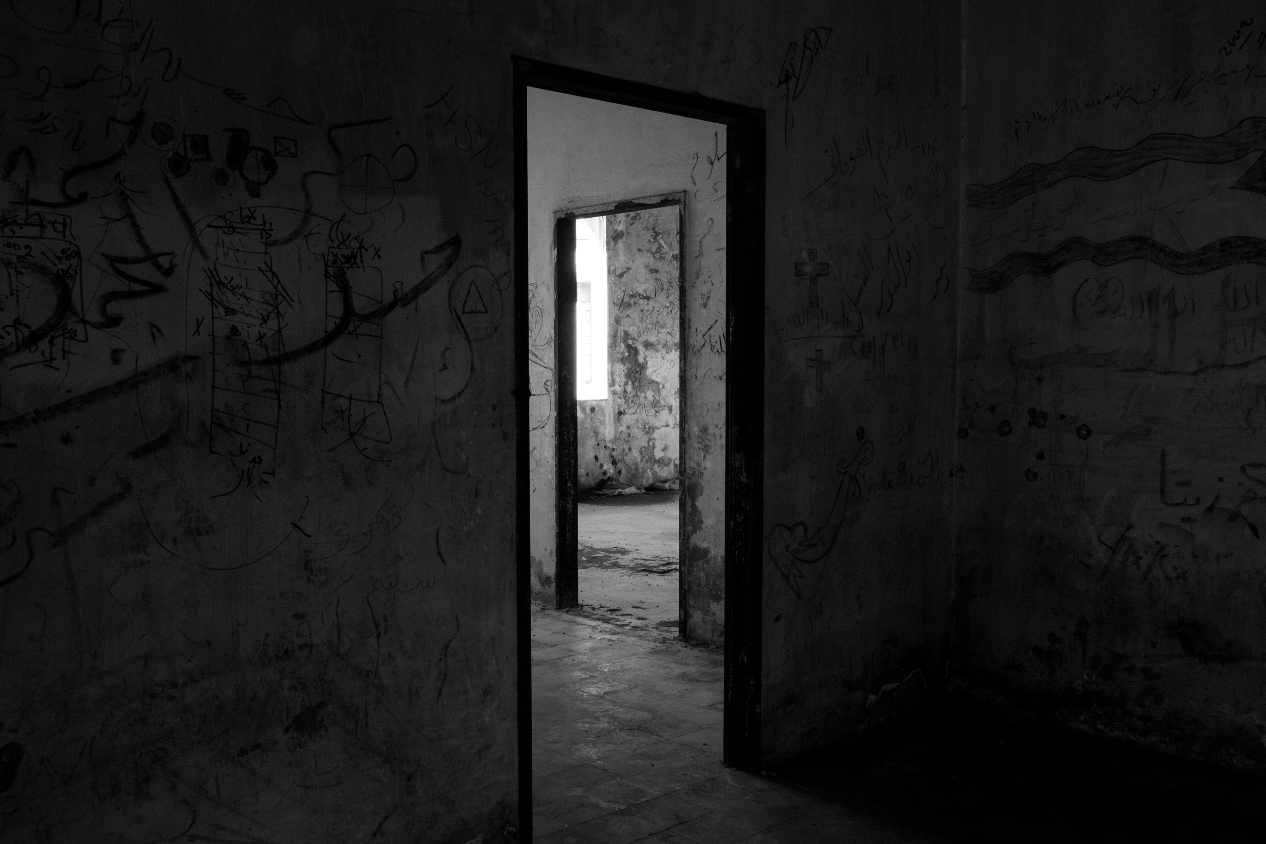 Dark, abandoned building interior with eerie shadows and graffiti-covered walls.