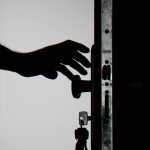 Silhouette of a hand about to open a door with keys in lock, symbolizing security.