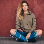 portrait young woman dressed hoodie ripped jeans leaning wall while sitting skateboard bridge footway 0.jpg