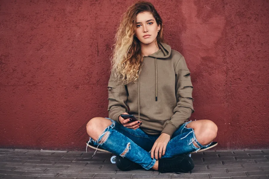 portrait young woman dressed hoodie ripped jeans leaning wall while sitting skateboard bridge footway 0.jpg